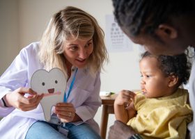 Odontopediatra realizando avaliação bucal em criança durante consulta preventiva para acompanhar o desenvolvimento dos dentes e da arcada dentária.