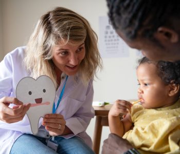 Odontopediatra realizando avaliação bucal em criança durante consulta preventiva para acompanhar o desenvolvimento dos dentes e da arcada dentária.