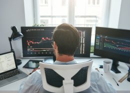 Trader acompanha gráficos do mercado financeiro em plataforma de negociação, representando o modelo de mesa proprietária e a formação profissional no mercado de trades.